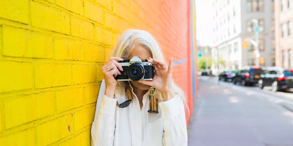 Mature woman leaning against a wall taking picture with a camera