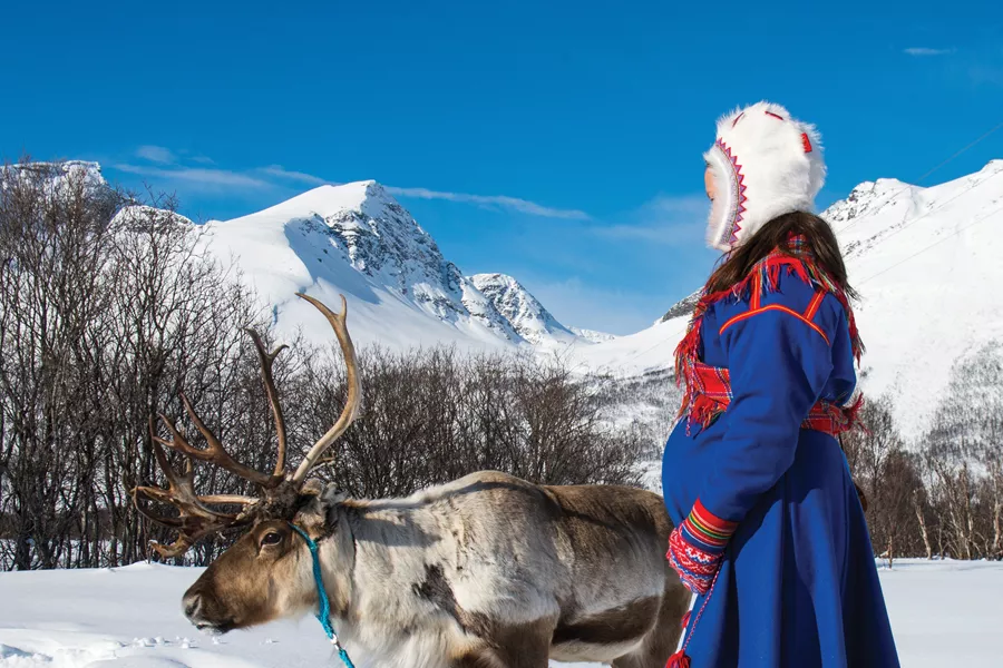 A woman and a reindeer surrounded by winter landscape
