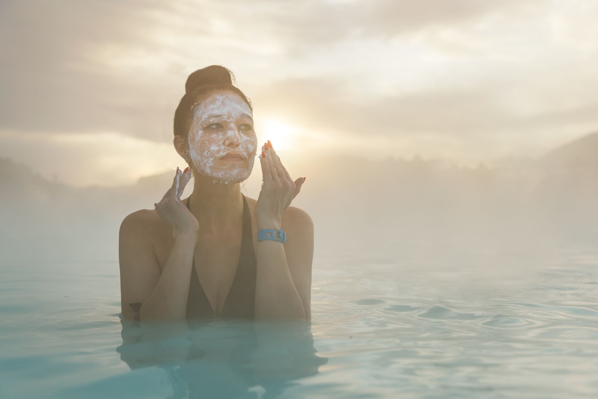 Woman standing in The Blue Lagoon nearing Reykjavik, Iceland putting mud on her face