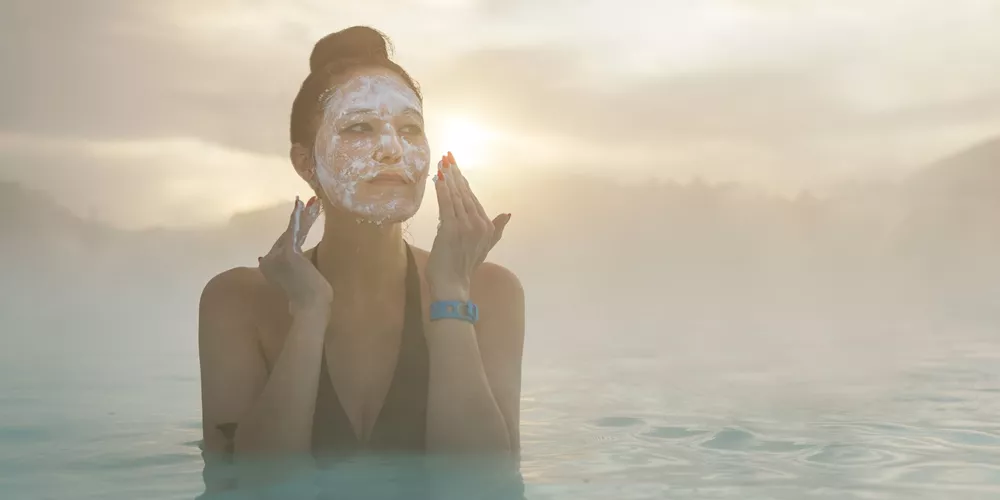 Woman standing in The Blue Lagoon nearing Reykjavik, Iceland putting mud on her face