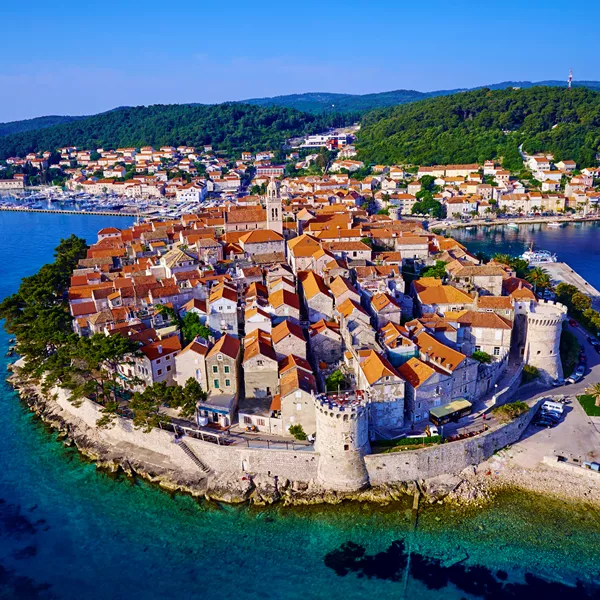An aerial view of the historic walled city of Korcula in Croatia, a labyrinth of stone streets and buildings with red tile roofs.