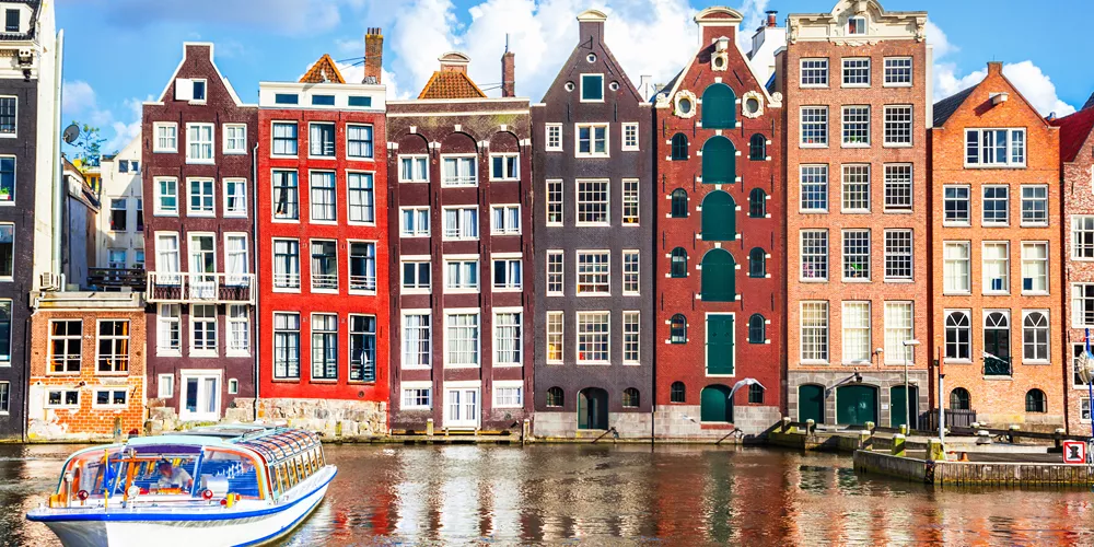 Tour boat cruising in front of multi-coloured houses in Amsterdam, Netherlands