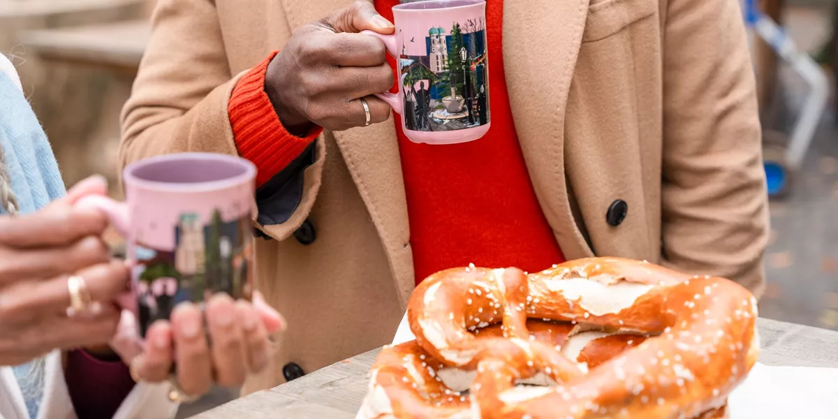 Guests holding Gluhwien and eating pretzels at a German Chrismtas Market