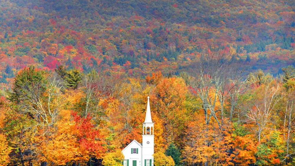 White church in front of autumnal trees during fall in New England