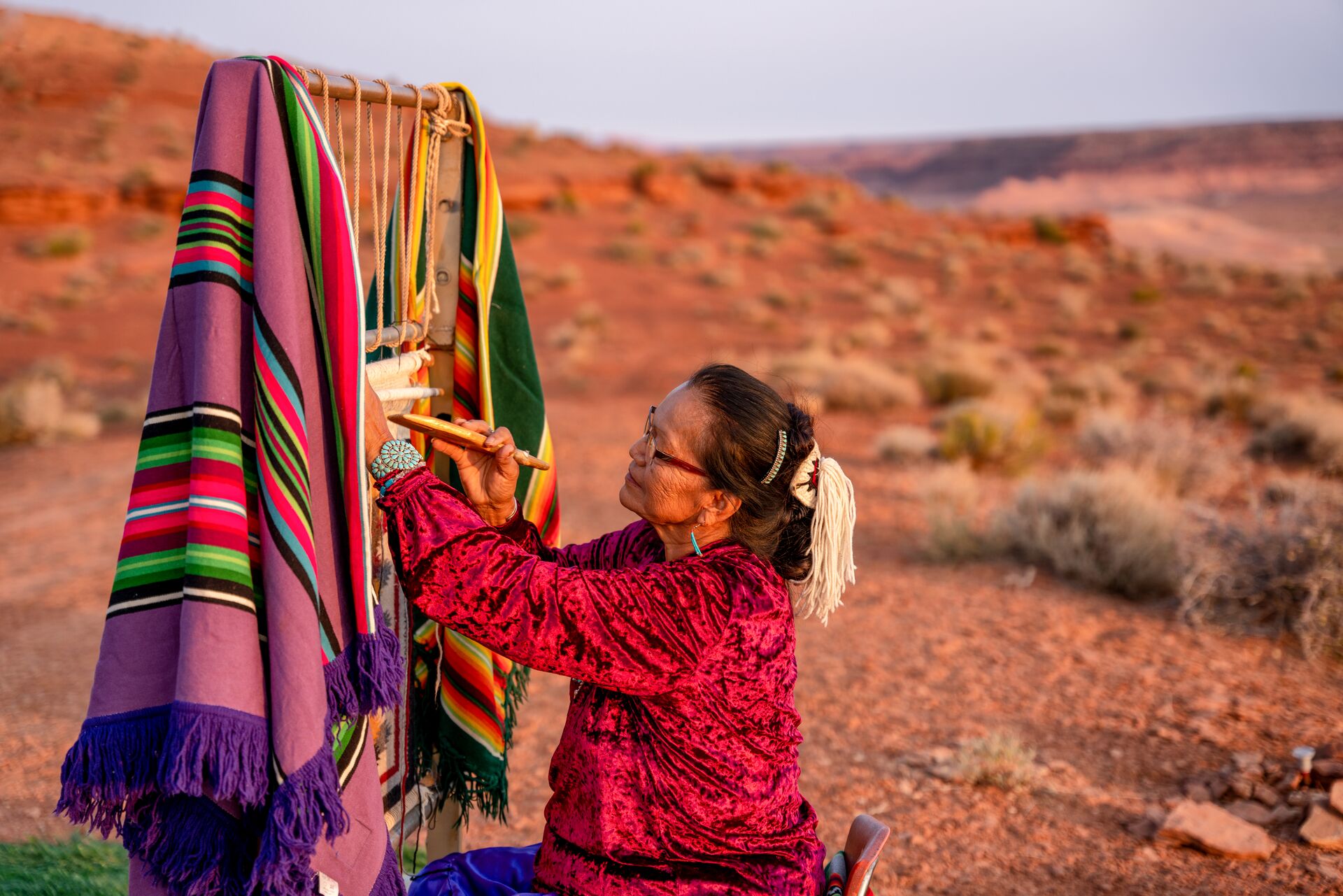 Large Elderly Navajo Woman Weaving A Traditional Blanket Or Rug On An Authentic Native American Loom In The Desert At Dusk Near The Monument Valley Tribal P 1278436213