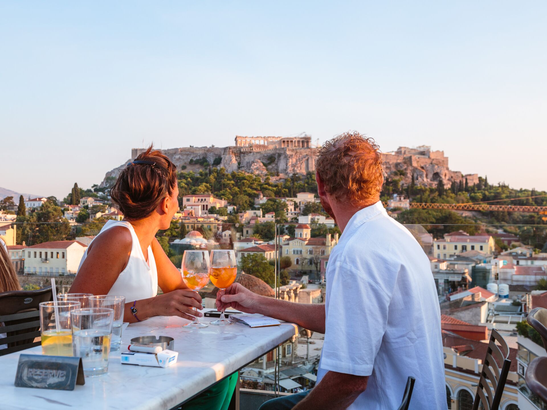 Couple drinking in front of the Acropolis at sunset in Athens, Greece