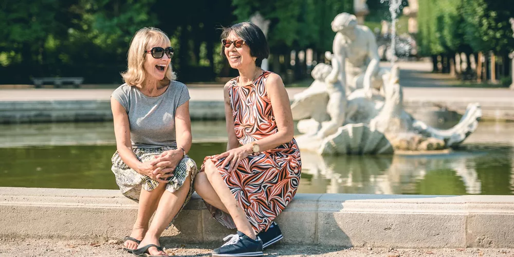 2 woman laughing while sitting next to a fountain in Schonbrunn Palace Gardens in Vienna, Austria