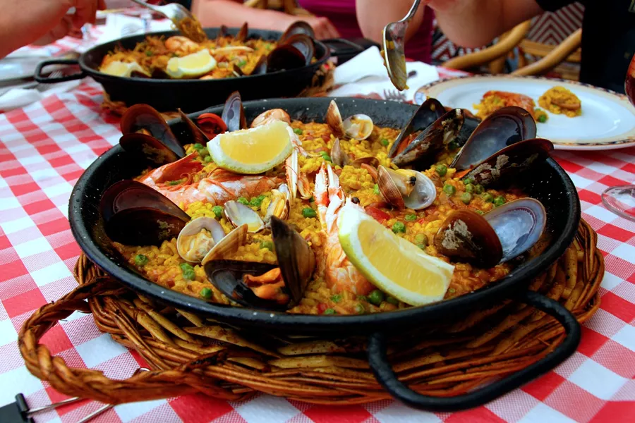 A black pan pf Paella on a checkered tablecloth