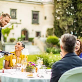 Guests sit at a table in the garden of a large house in Italy