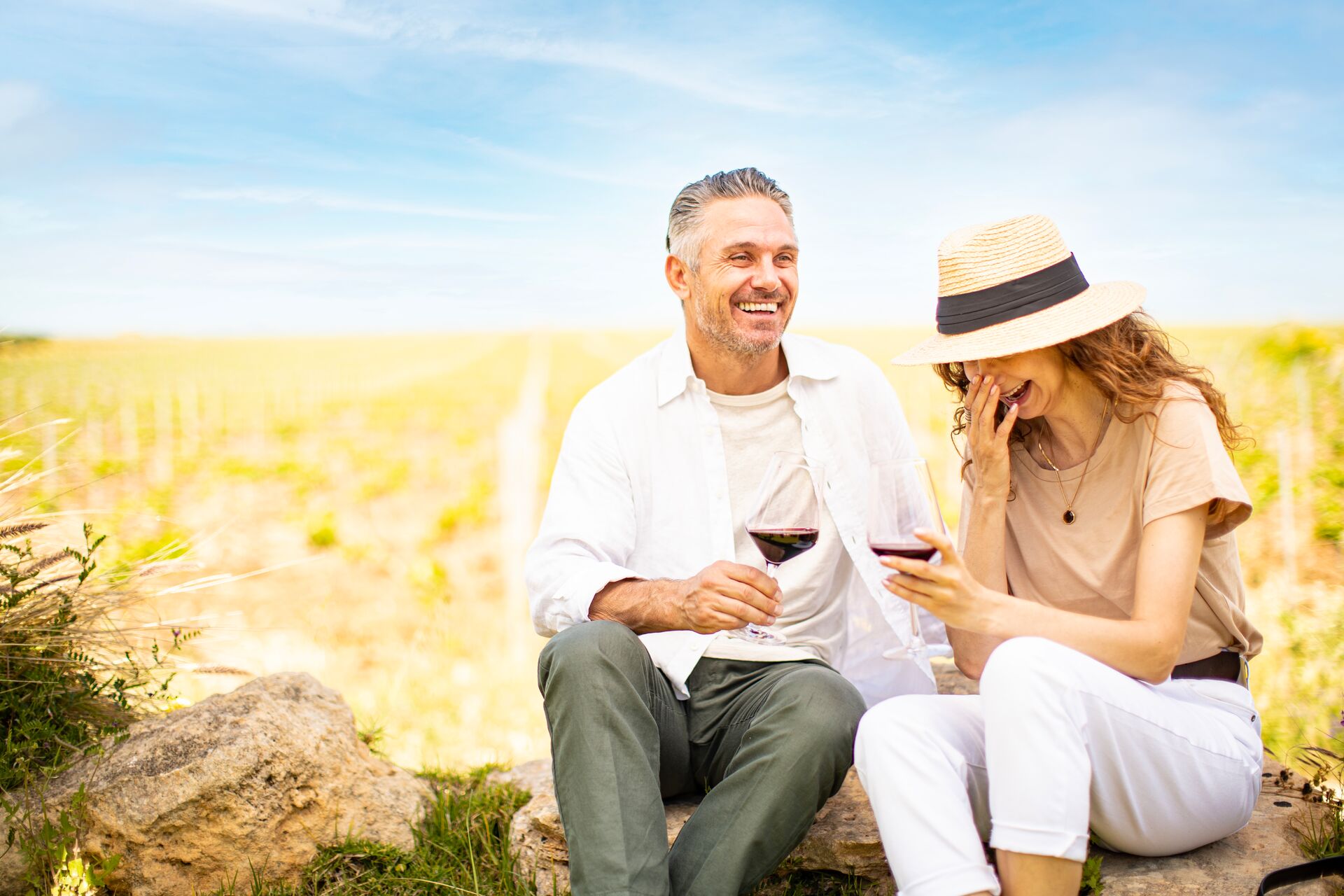 Two guests on tour drinking wine and smiling outdoors in field