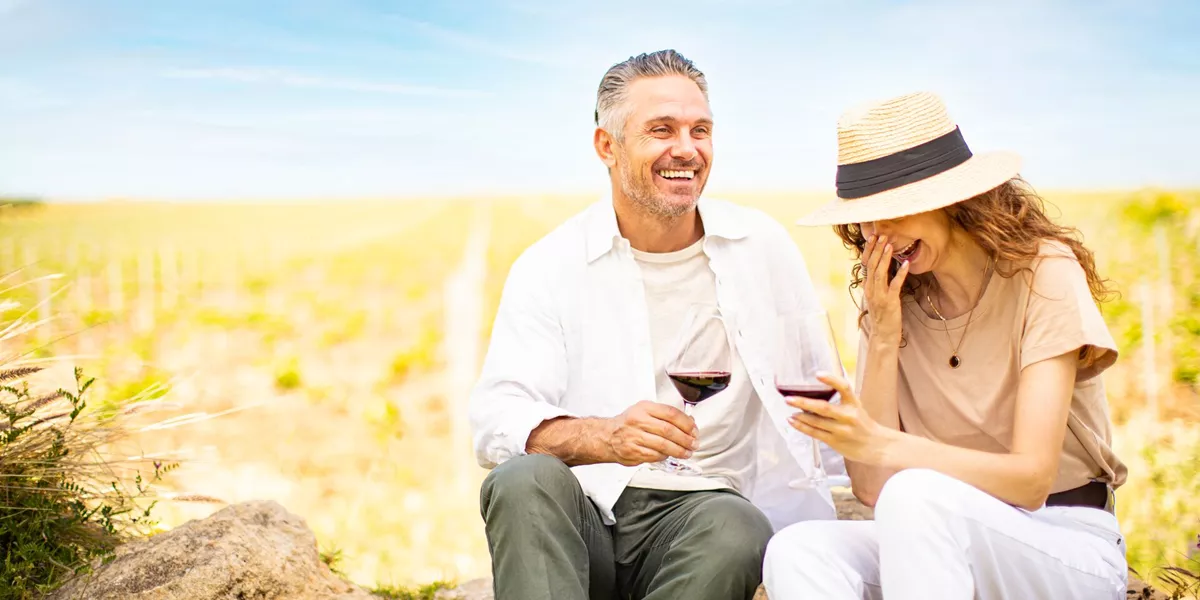 Two guests on tour drinking wine and smiling outdoors in field