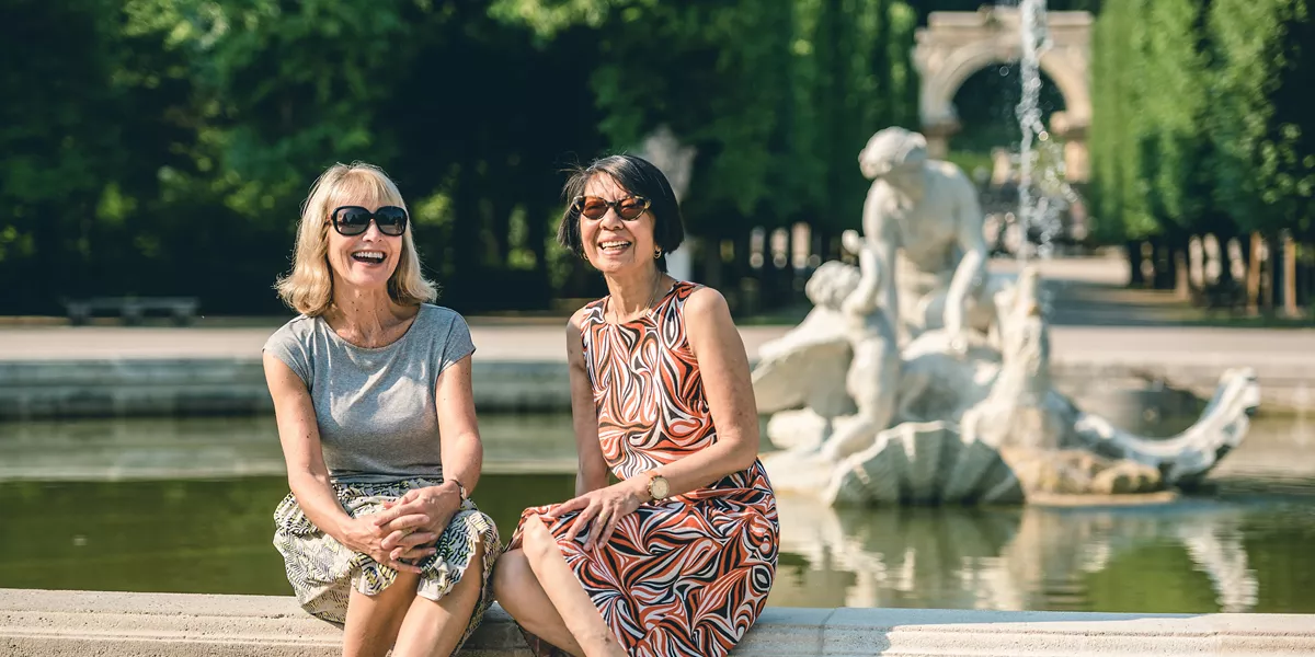 Two women sitting on a fountain and smiling.