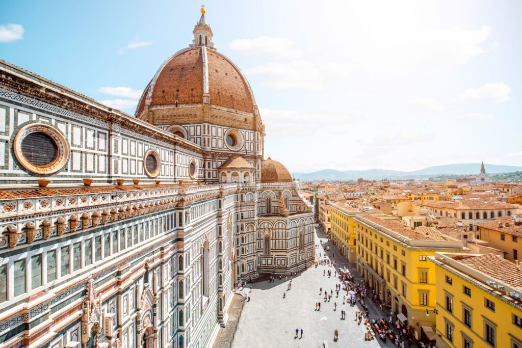 View from the roof of a red and white brick palace in Florence, Italy, down over the golden buildings of the city.