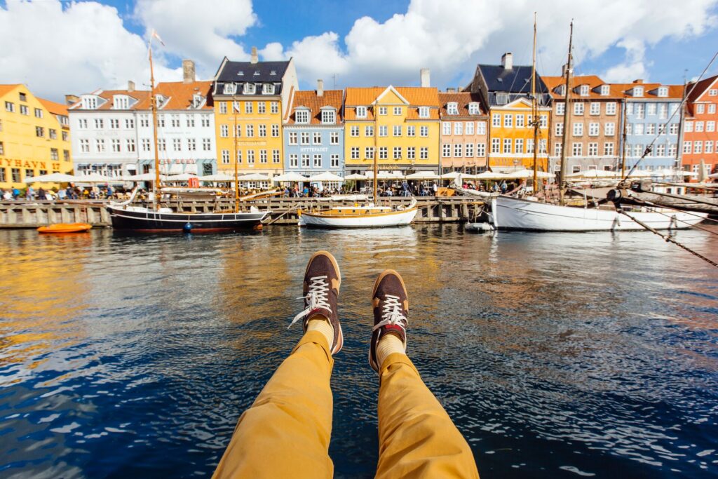  Pov shot of legs stretching over a Copenhagen canal, a row of colourful houses makes up the background