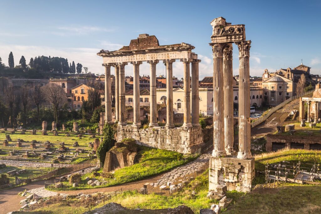 Huge stone columns stand with green grass and the city of Rome, Italy, behind.