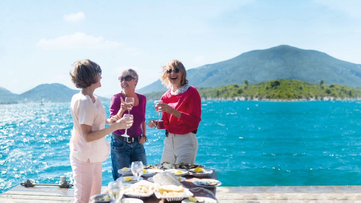 three women enjoying wine and oysters by the ocean