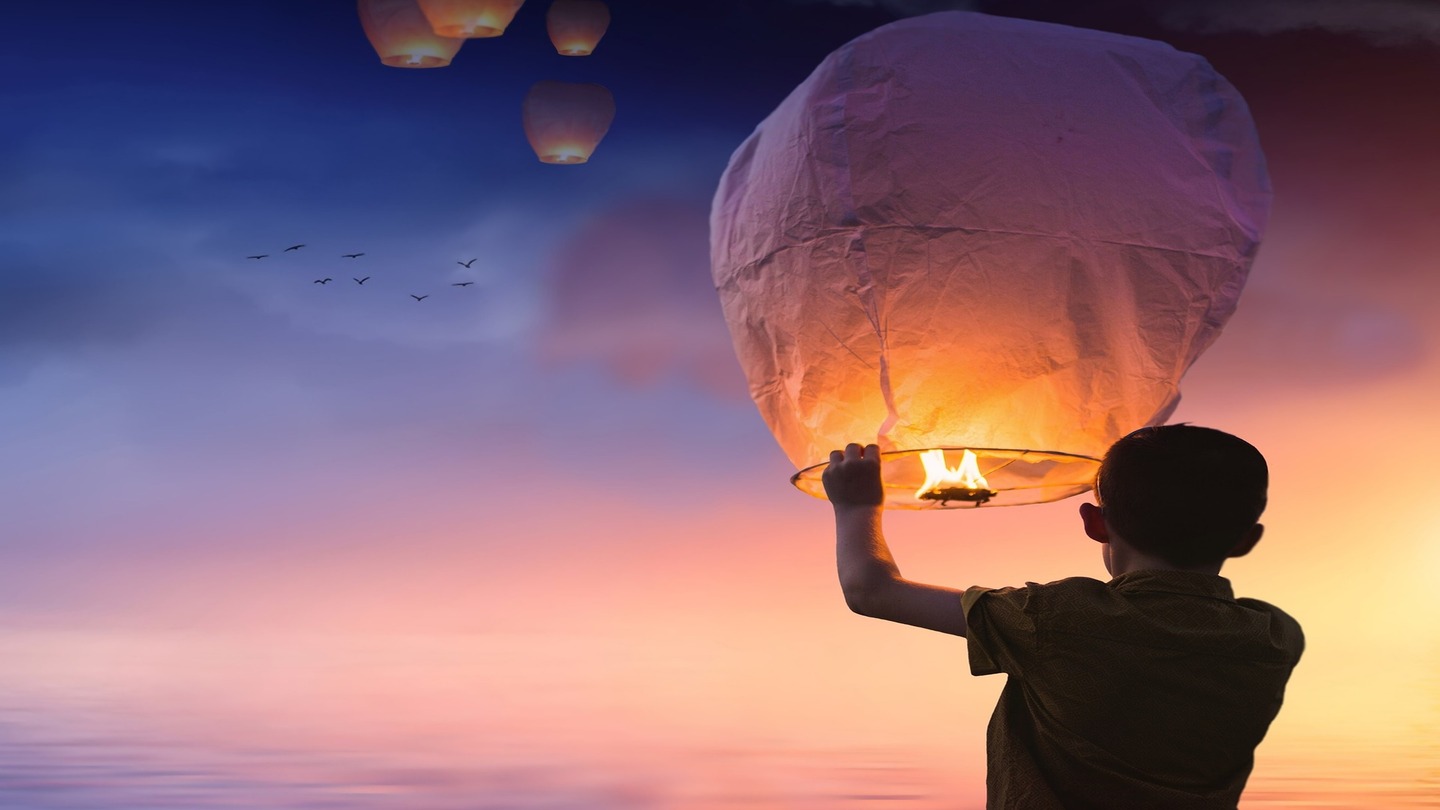 person releasing a lantern at sunrise