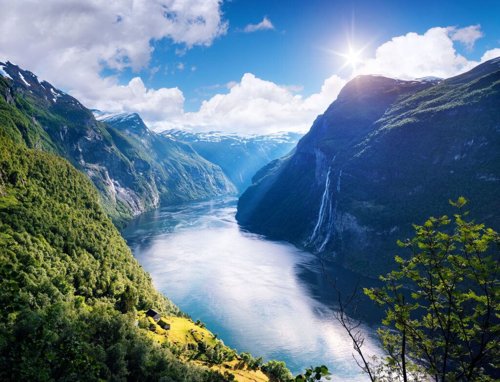 Aerial shot of geirangerfjord in Norway, with clouds resting down not he water and steep, green mountains either side.
