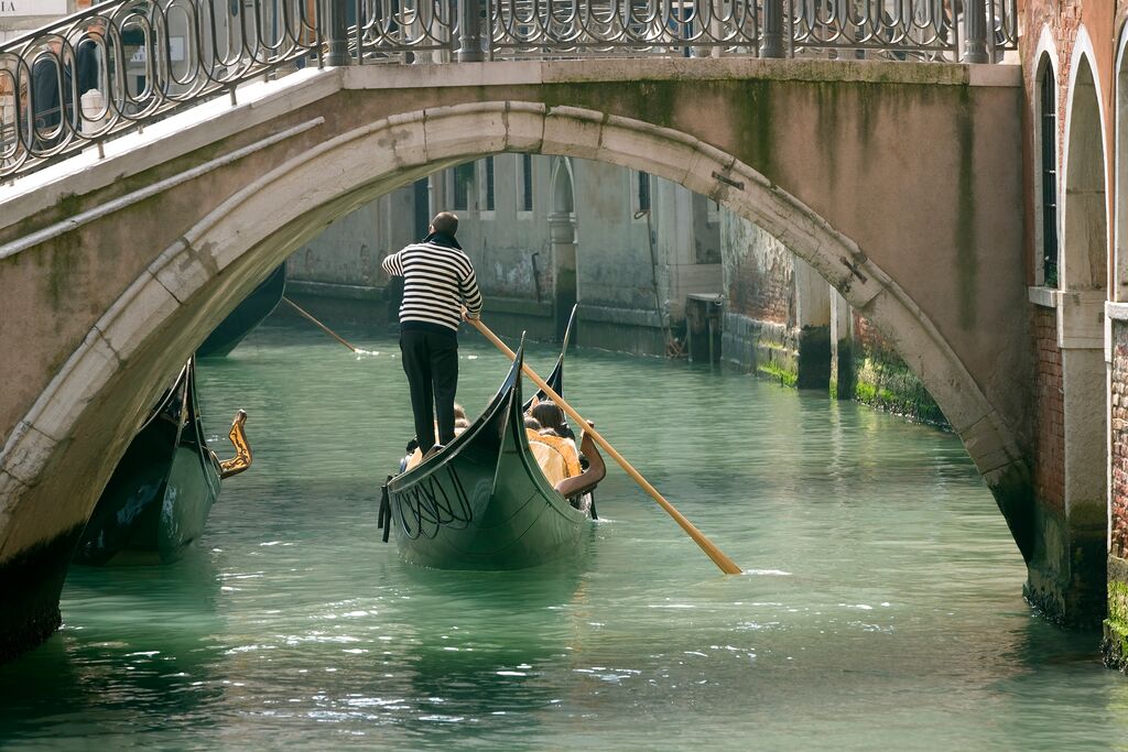 A gondolier pushing his gondola along a canal in Venice, framed by an archway