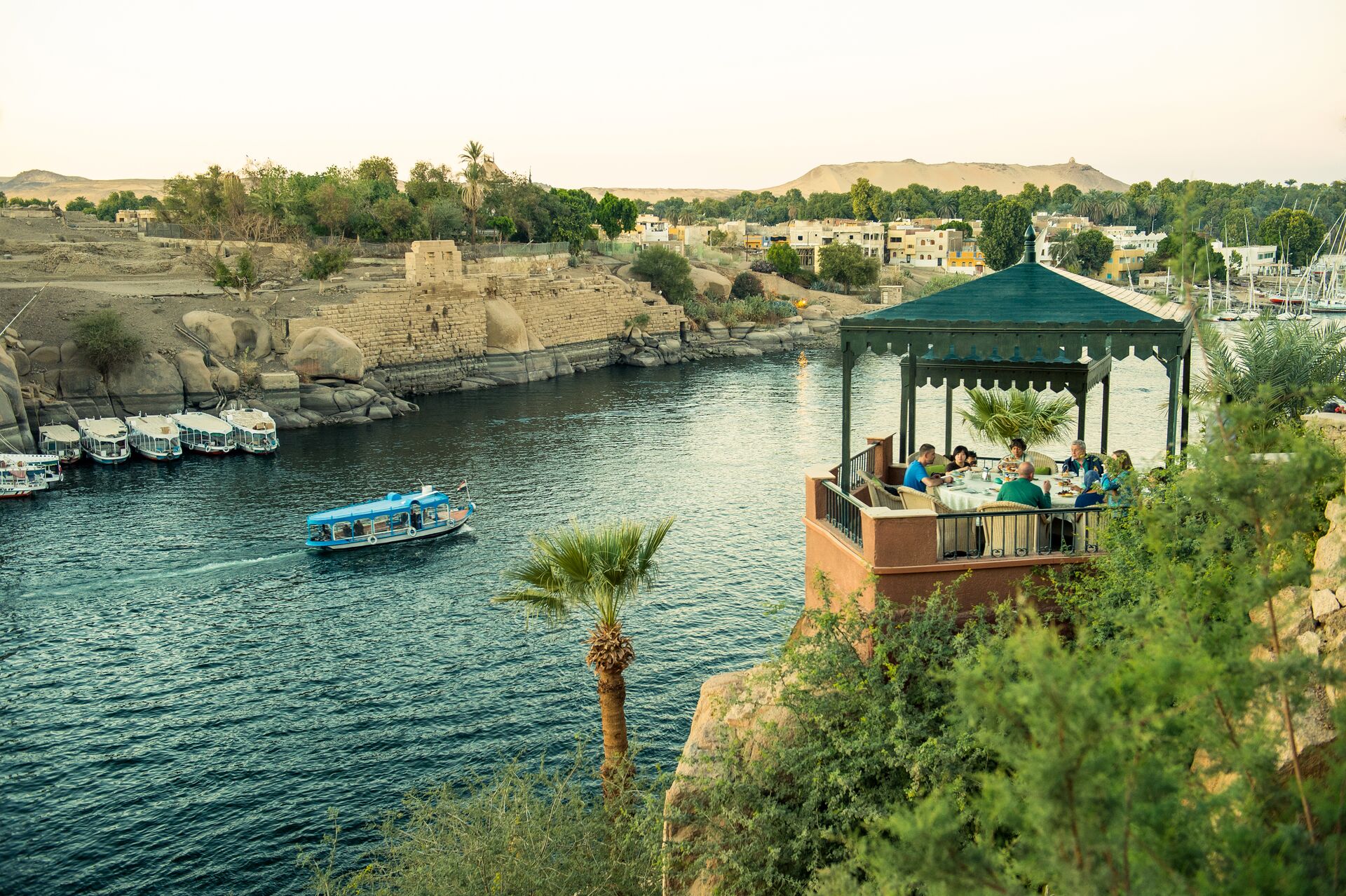 Image showing the view of the river Nile from the Old cataract Hotel. Showing guests enjoying tea on a terrace beside the river, with a boat and archeological ruins in the background.