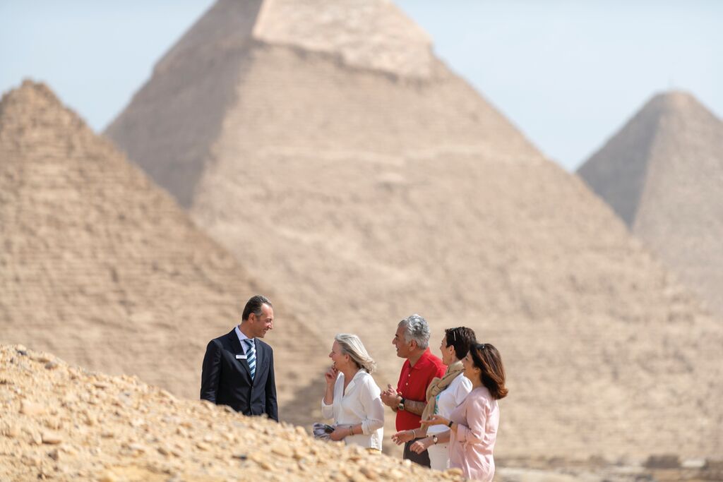 A group of people talk while the pyramids of Giza tower in the background.