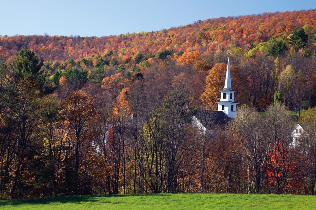 Rainbow coloured forests sprawl out into the distance, with the white steeple of a church poking out from between the trees. Sights like these make New England one of the best places to visit in September