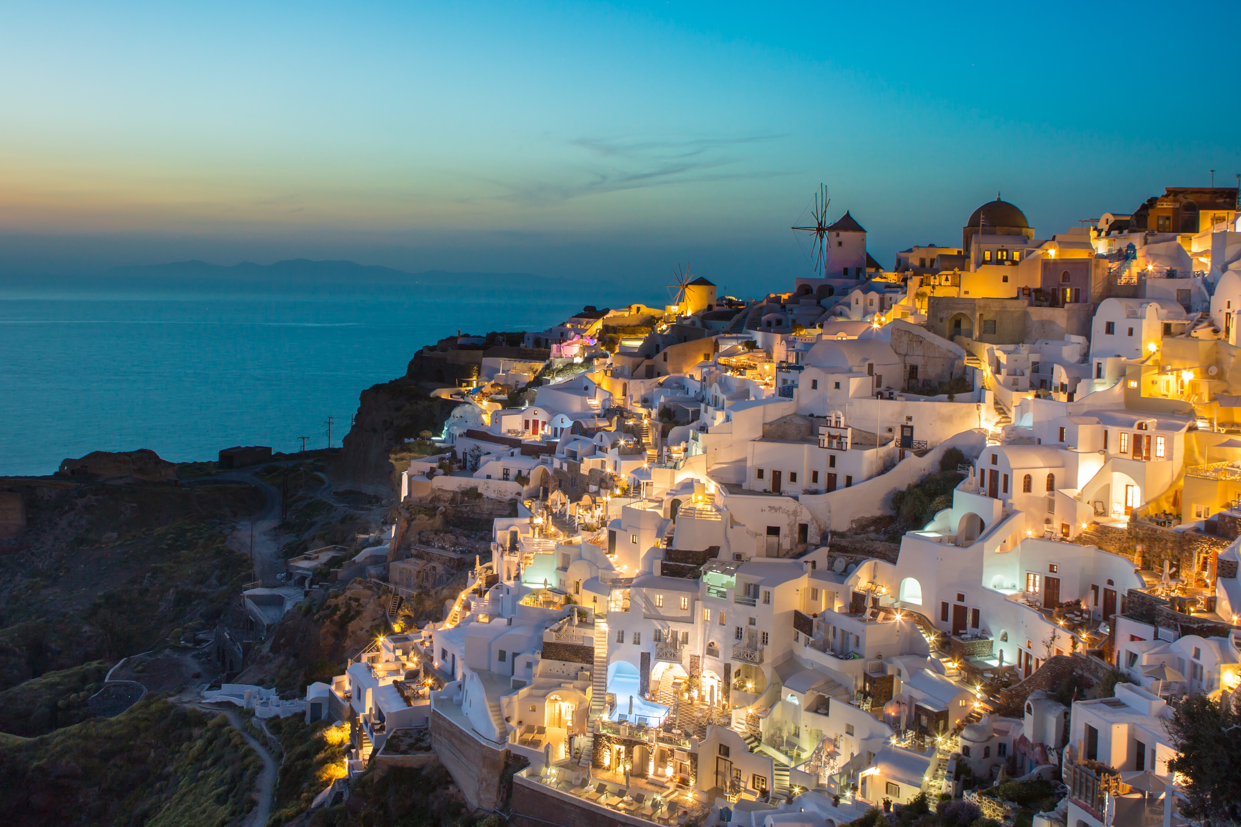 Santorini's white building lit up during golden hour, the sun setting in the horizon. Sights like these make it one of the best vacations in September