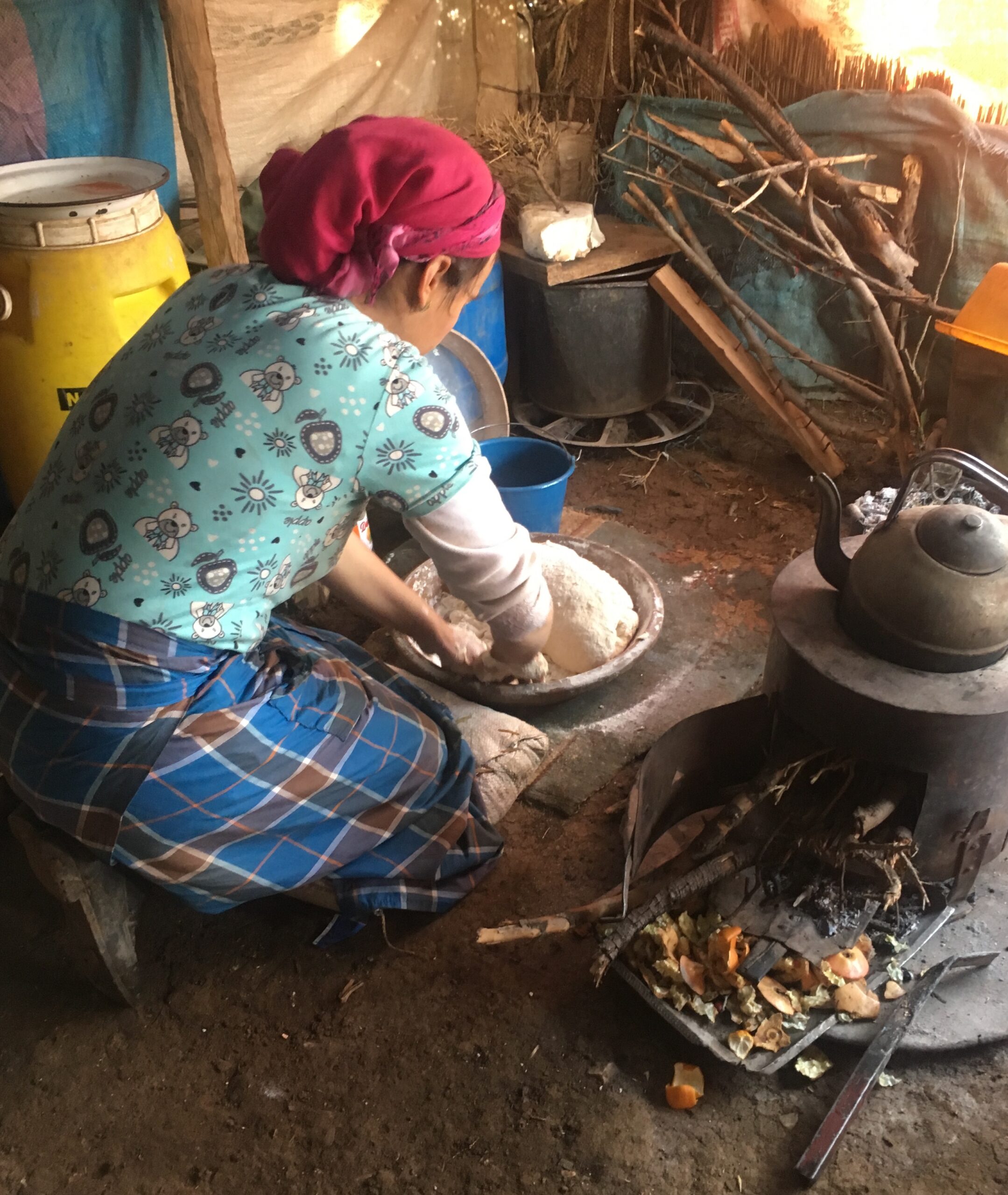 Image of Fatima, crouched down preparing bread with her traditional oven in a basic kitchen