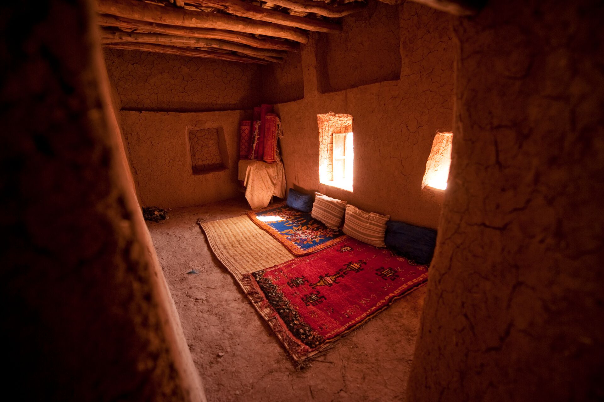 Image of a traditional Berber hours, showing a basic room with colourful mats and pillows on the floor