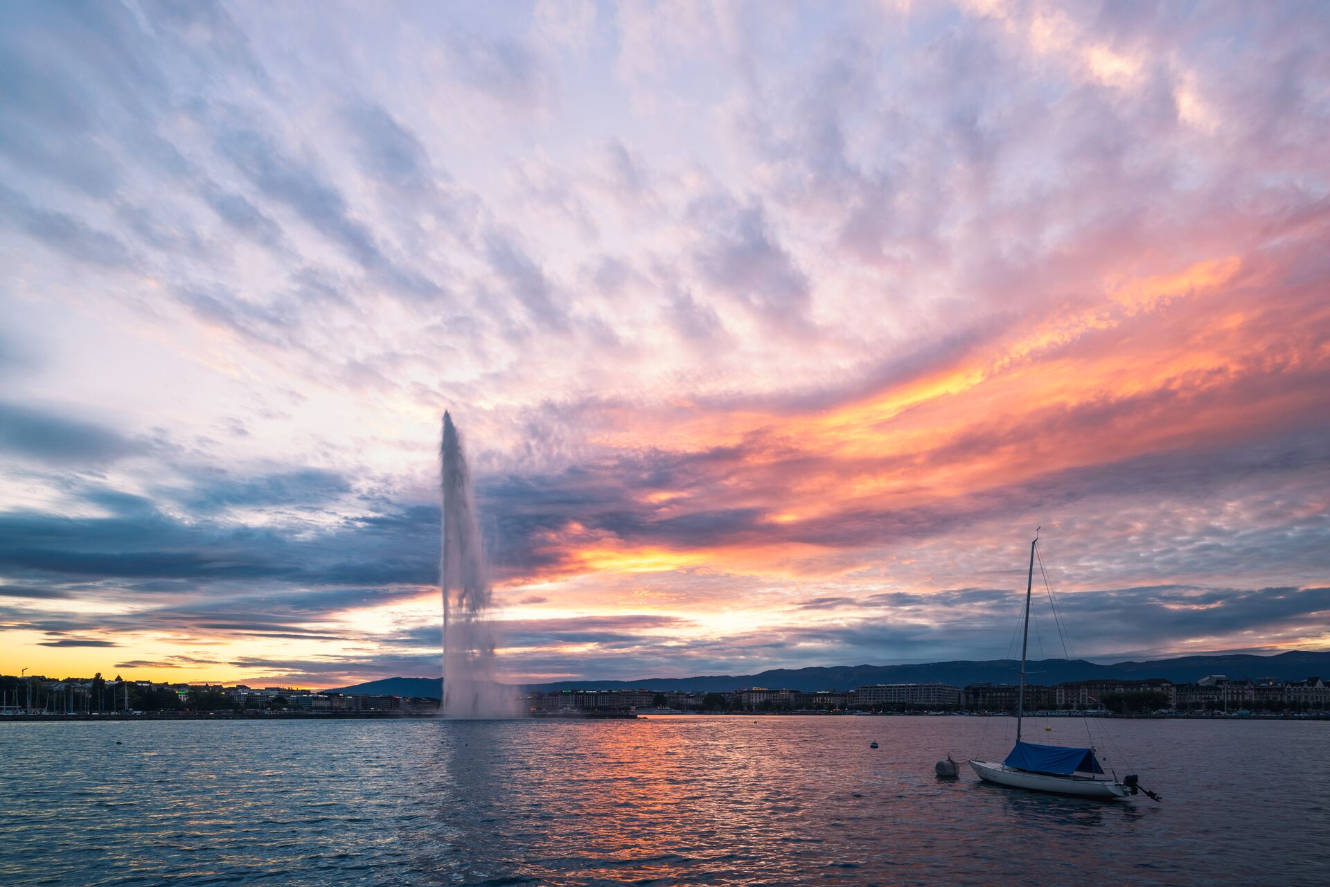 Image of blue Lake Geneva showing the warm colours of sun set over the Jet D'Eau