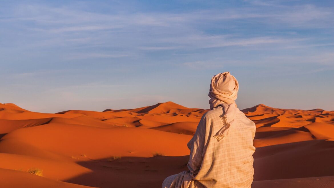 Image of Berber man sitting down, from behind as he overlooks the Sahara Desert