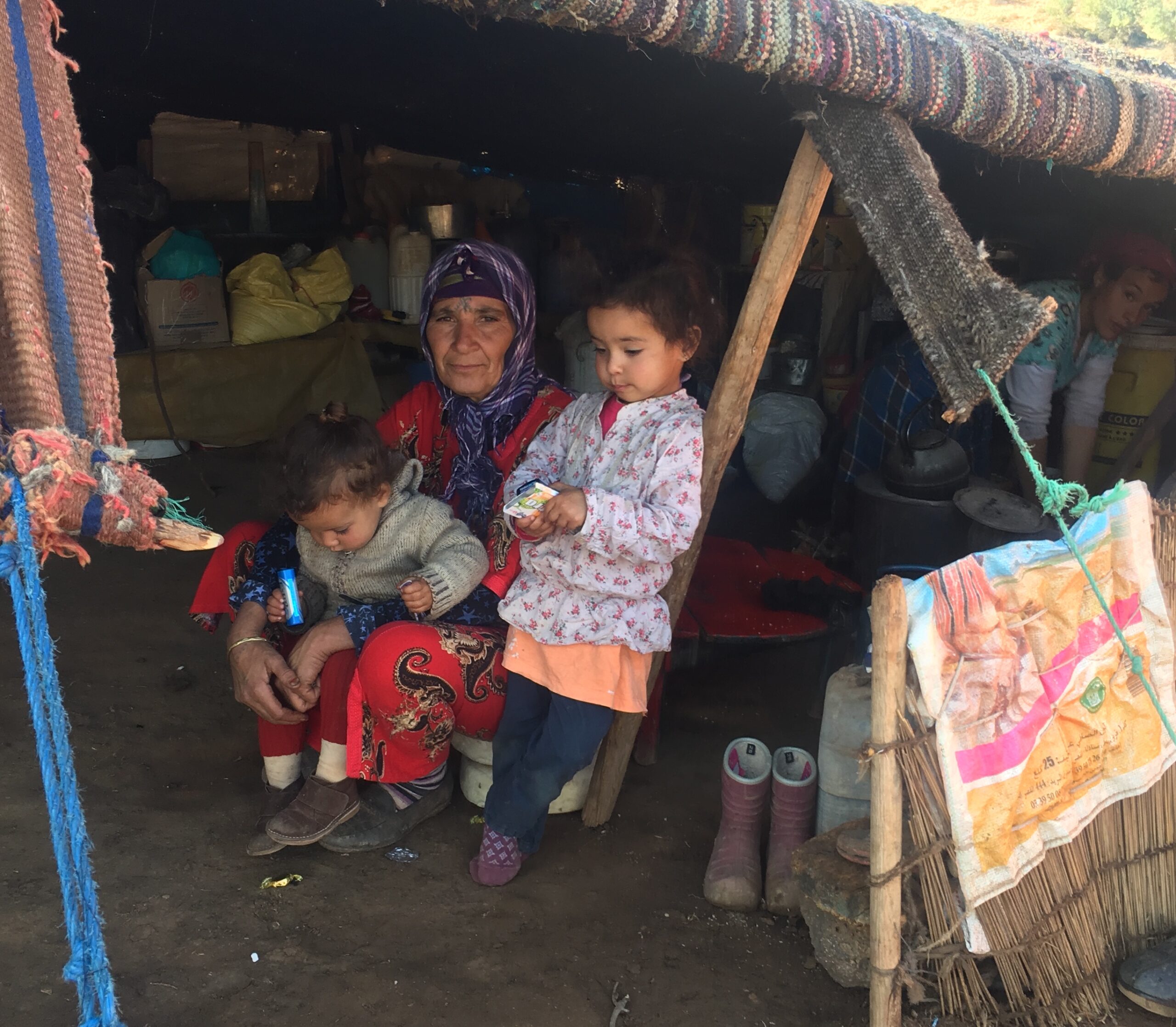 Image of Zahra, a berber, with her two grandchildren by her side, with her traditional house in the background