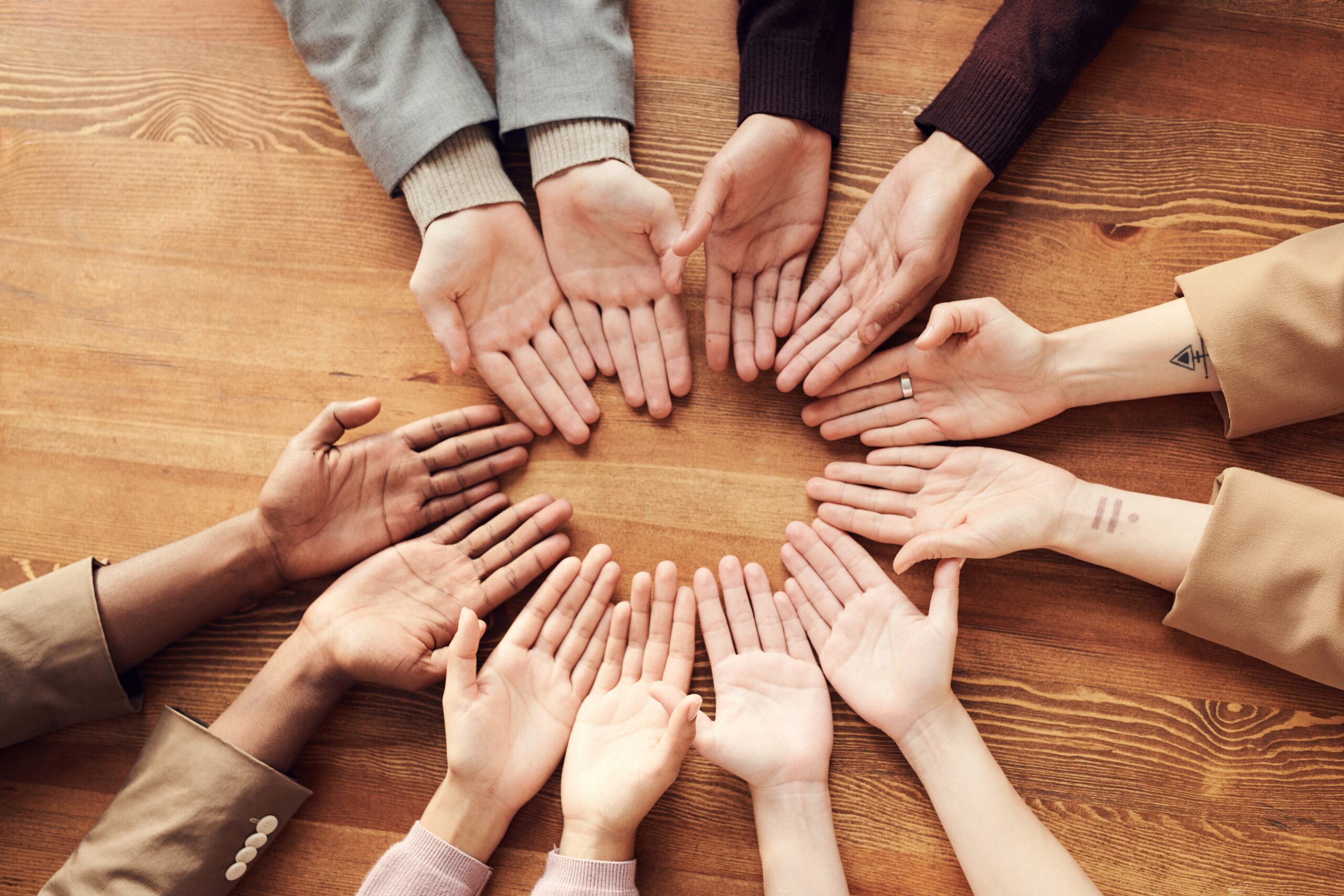 Image of hands, in a circle on a table showing different sexes and ethnicity