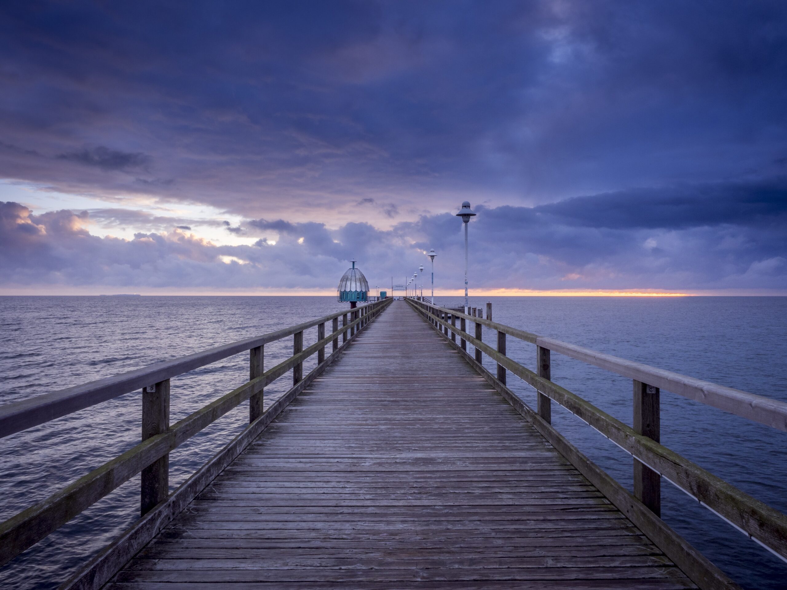 Image of pier boardwalk with blue sky and blue water below.