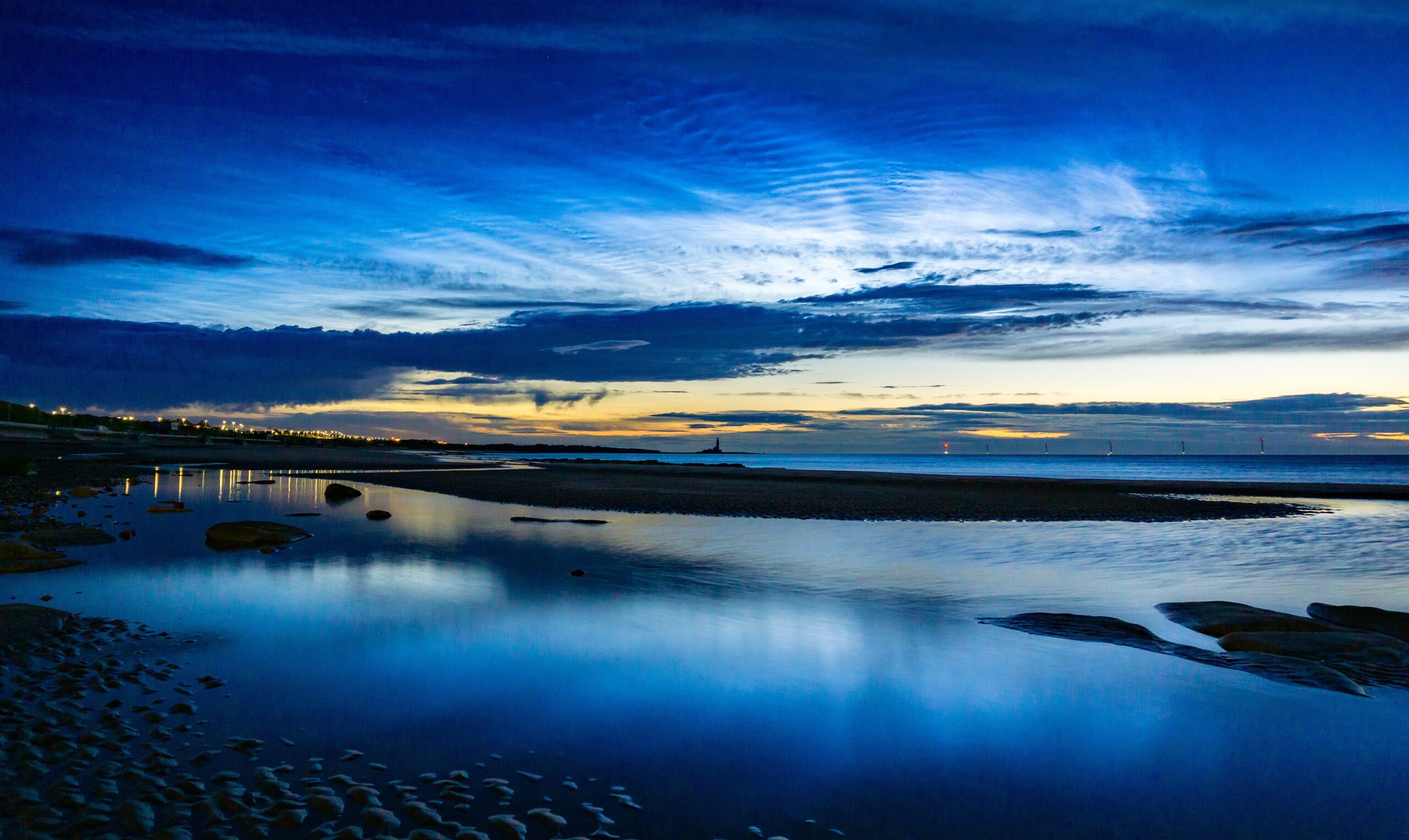 Wide generic image of sands in the evening, with water still sitting, iridescent blue looking out to see and the sky.