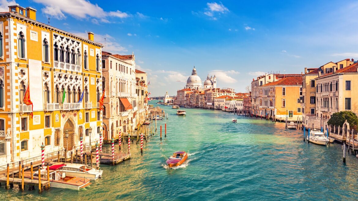 Venice on a sunny evening showing ornate and colourful buildings against the green waters of the canal with a boat passing through