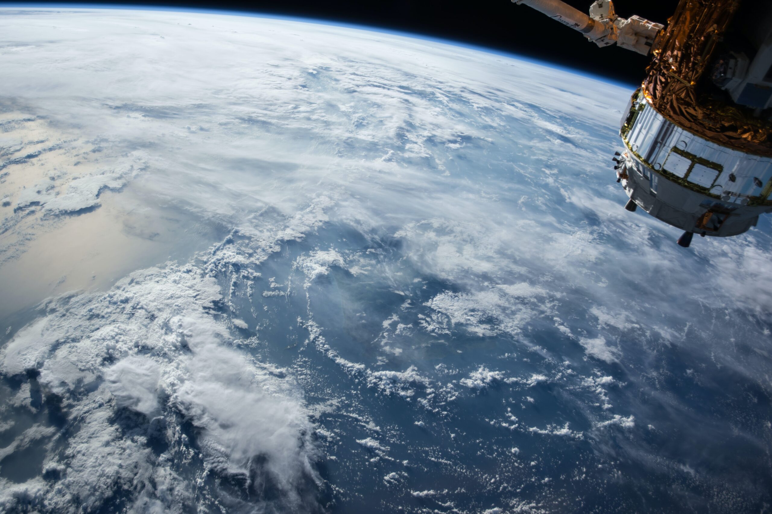 Image of earth taken from space whopping clouds and blue surface, with a spacecraft in the top right corner