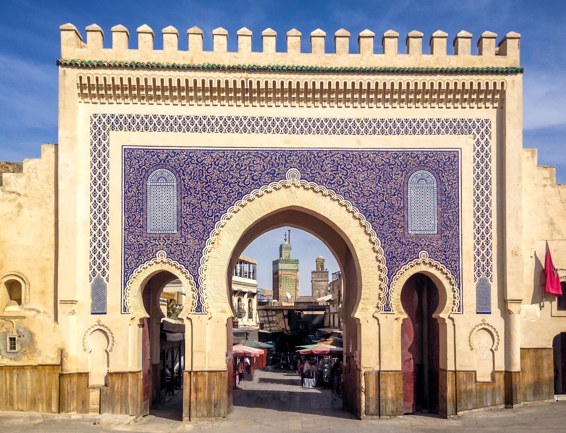 Large, ornate blue and while gate to the Fes Medina, with three archways showing the old town behind.