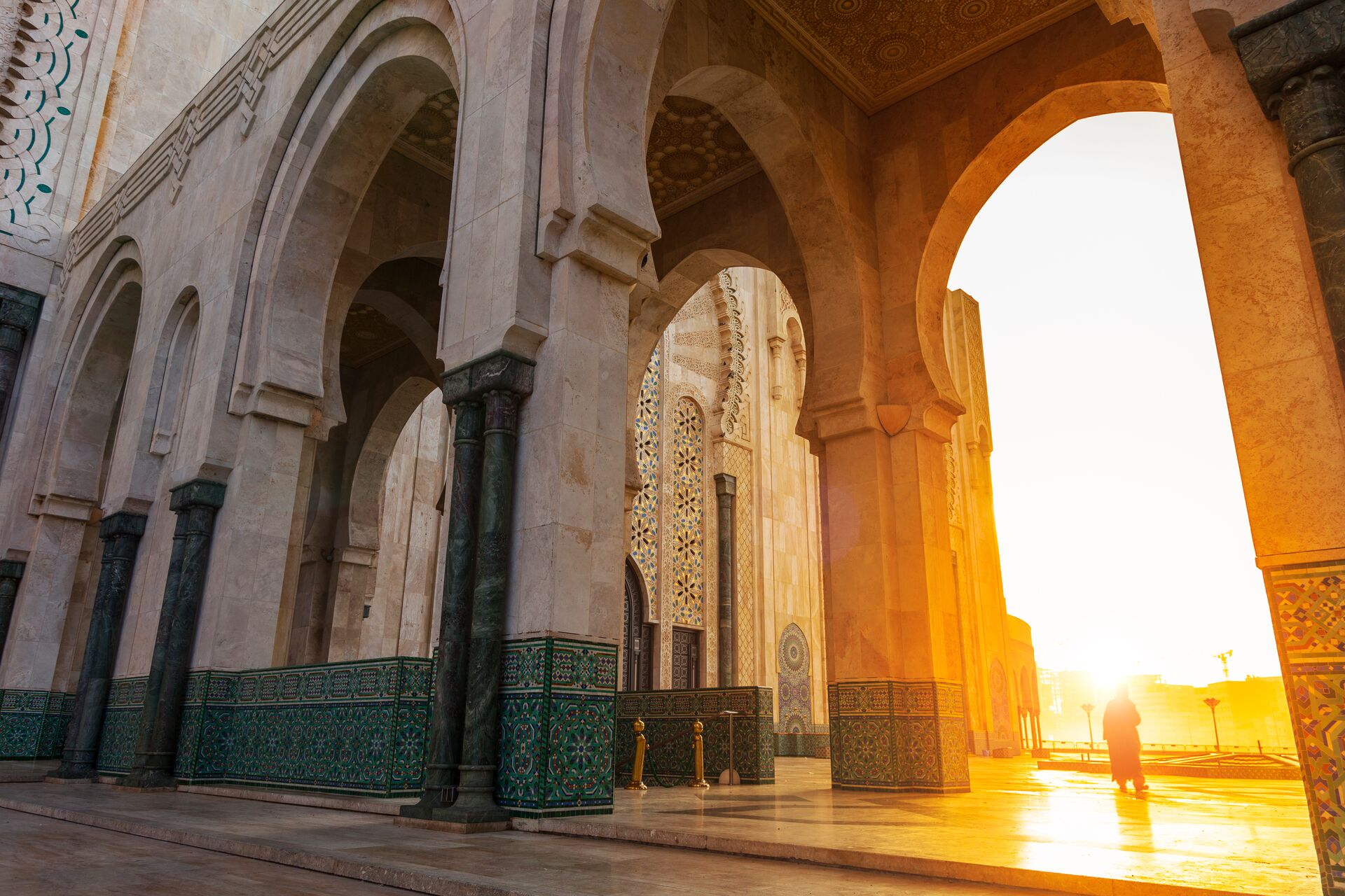 Hassan II Mosque in Casablanca, showing whits stone pillars and archways with the sun in the background