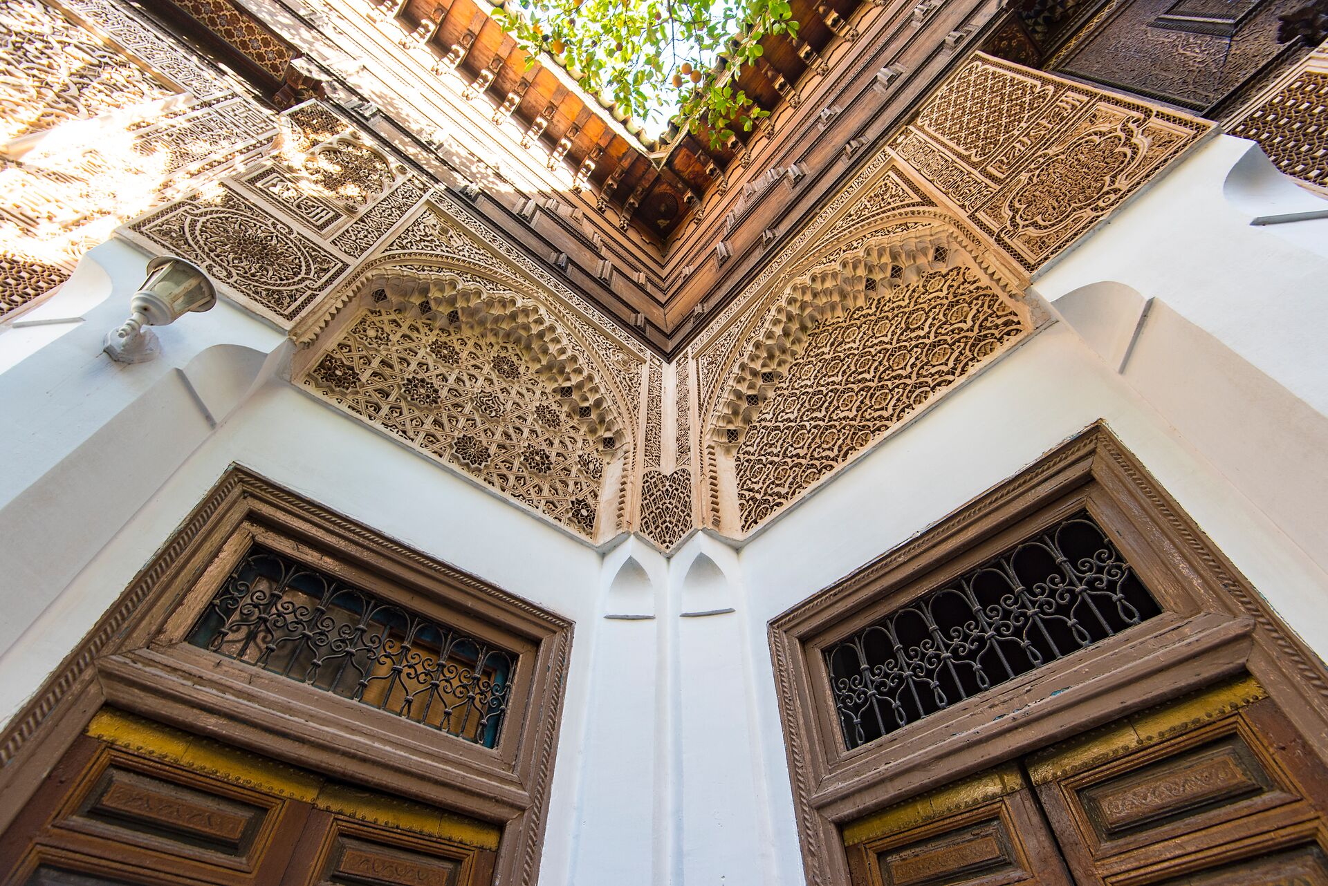 a view looking up at ornate wooden trelliswork and red roof tiles of the Bahia Palace in Morocco
