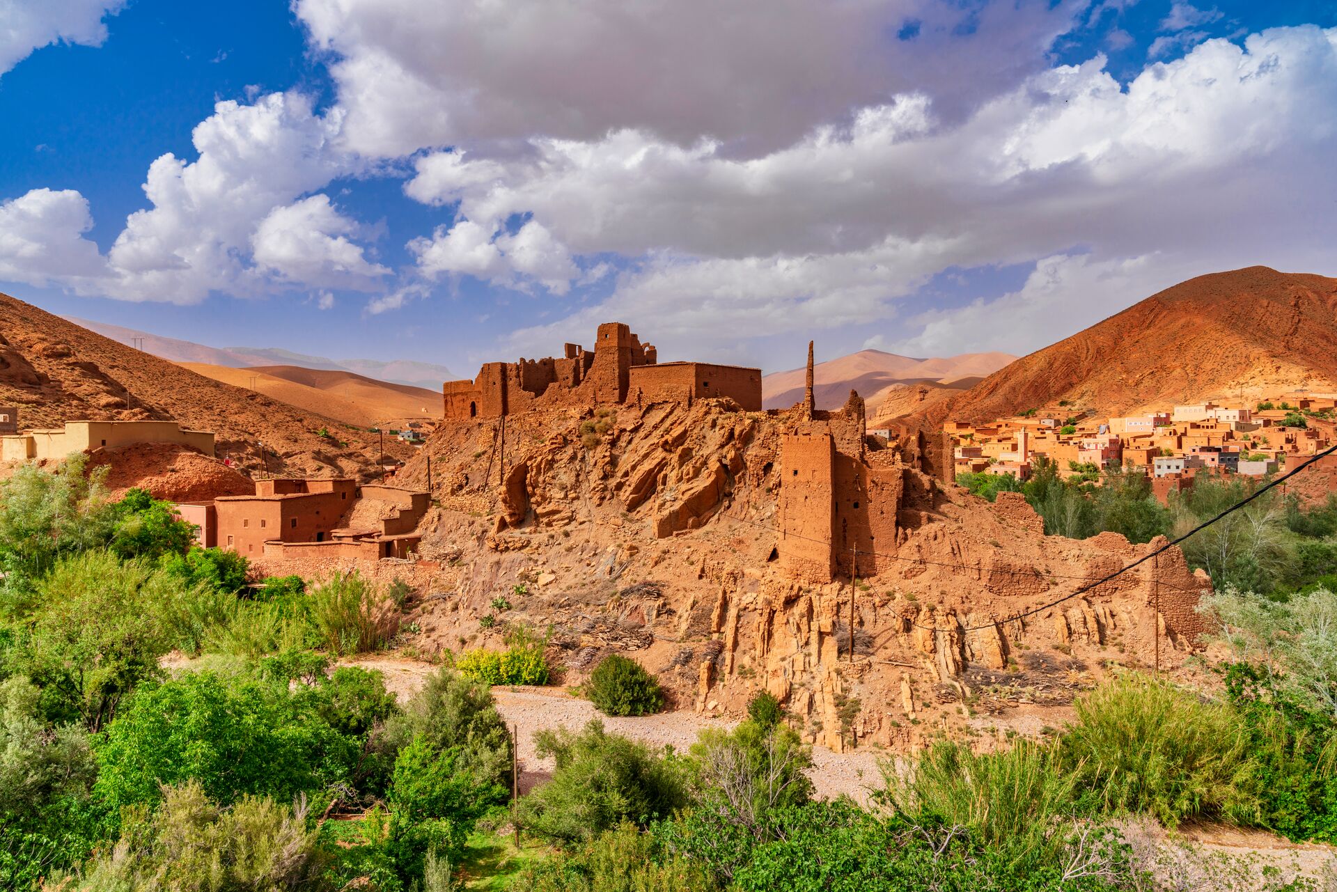 Res stone houses, mountains and green vegetation of Daded valley in Morocco, with lots of white clouds overhead