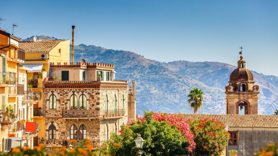 Sunshine view over Taormina with yellow buildings in front and mountains behind, showing the spectacular architecture