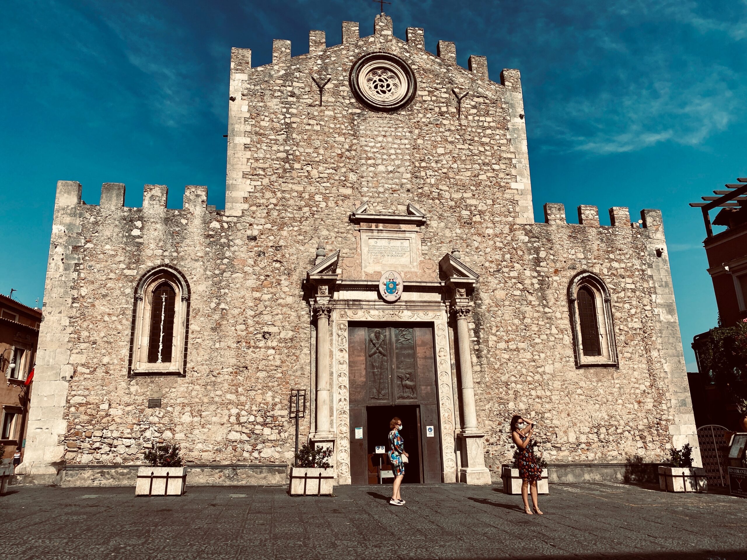 Close up of the white and grey stone facade of the Duomo di Taormina, quite simple and elegant, against a blue sky
