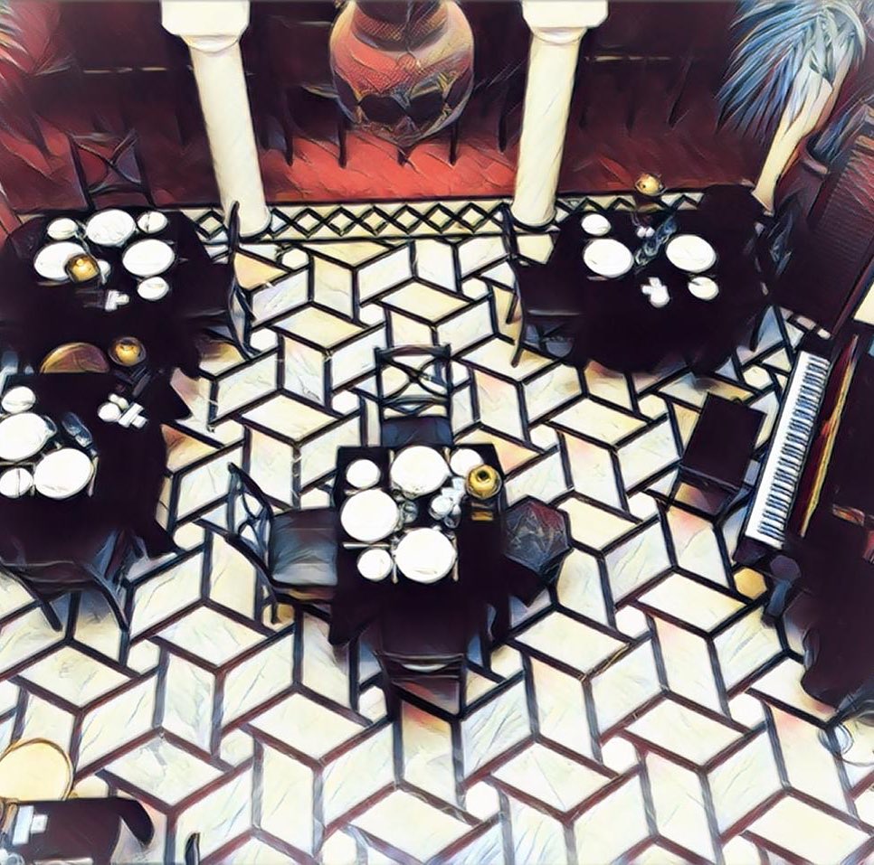 Picture taken looking down on black and white tiled floor with black tanks and chairs, white crockery all laid out and a piano