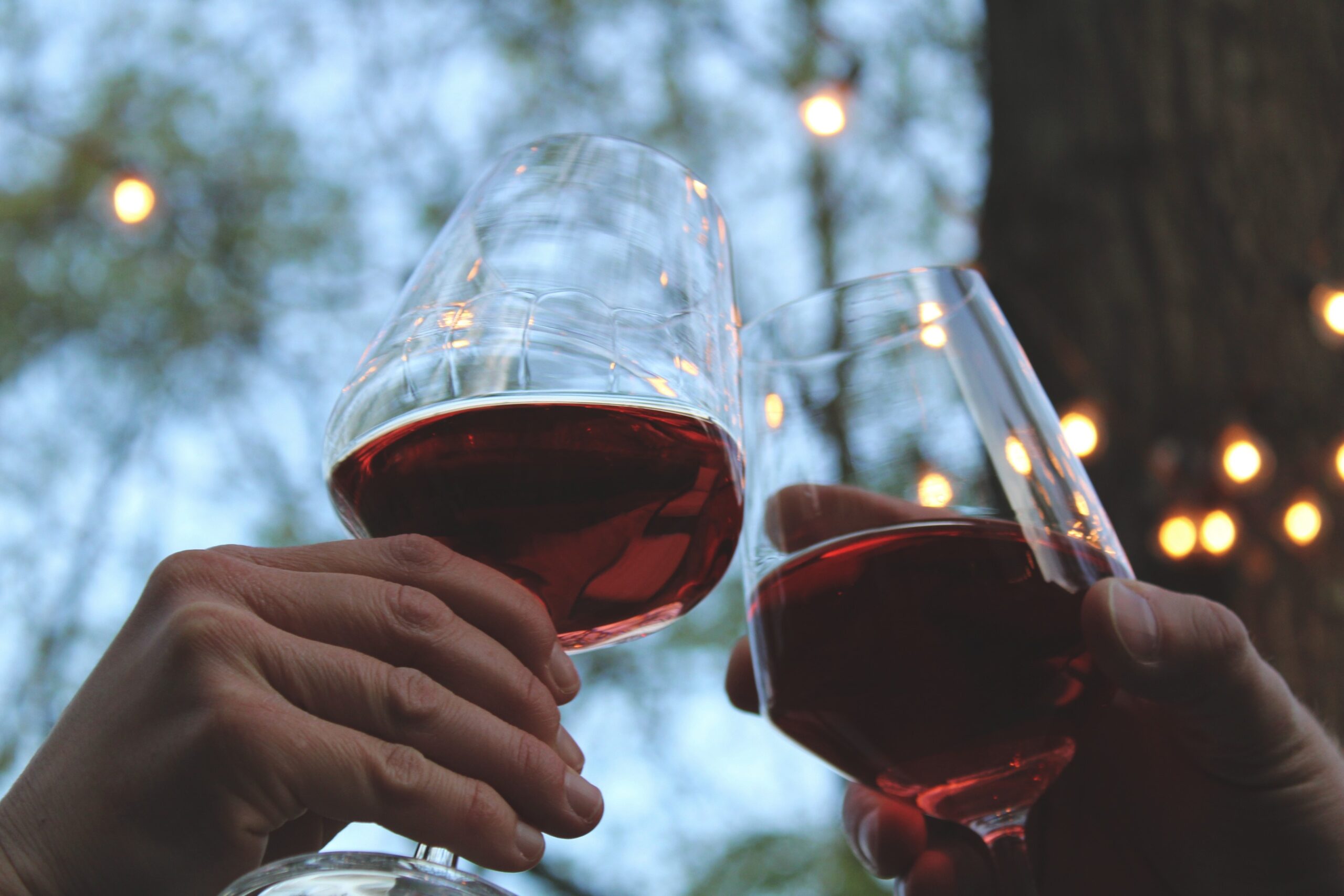 close up of hands clinking two glasses of red wine together, with a blurred background