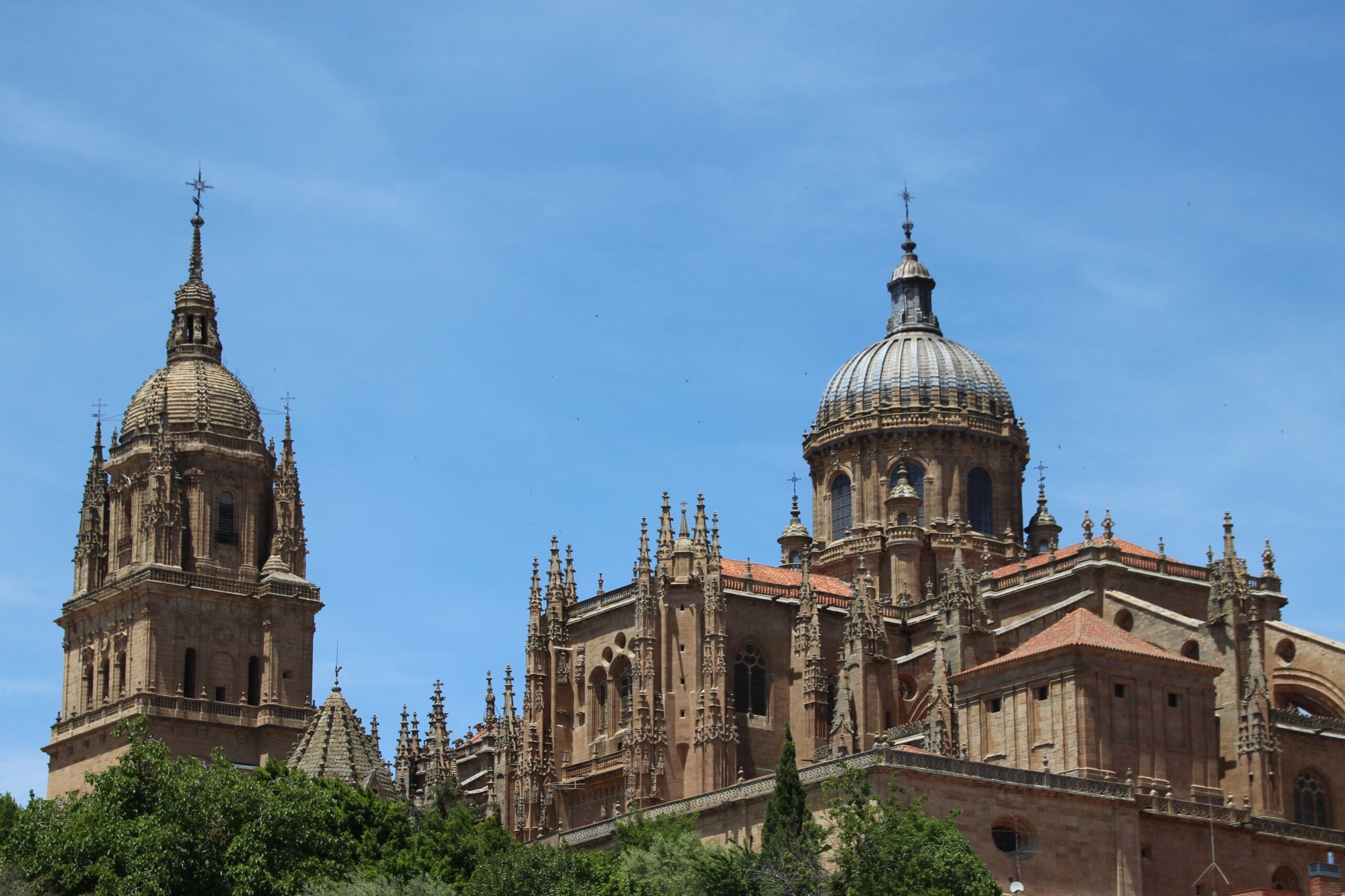A domed roof with a spire of Salamanca’s New cathedral stands ornately against a bright blue sky