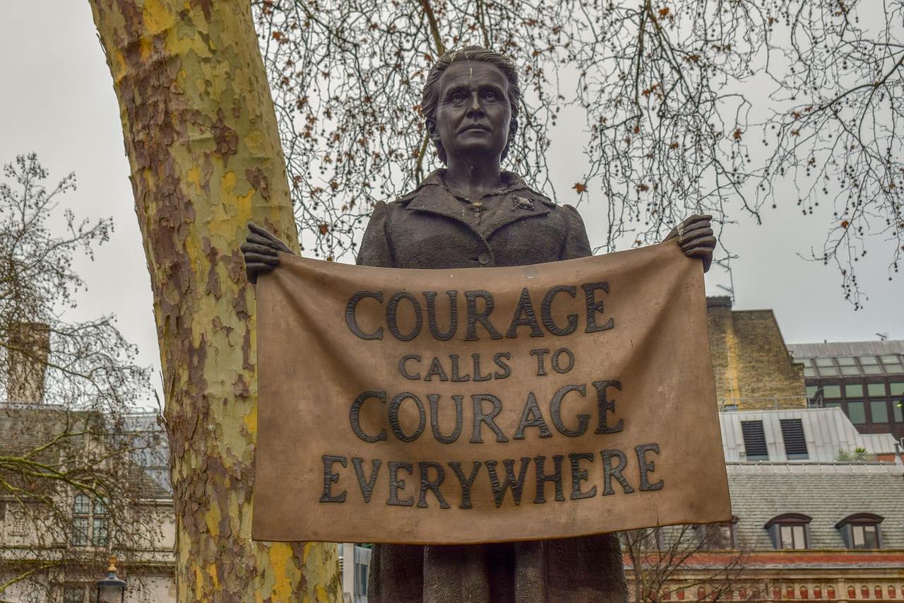 Photo of a statue of a Suffragette holding a banner that reads 'Courage Calls to Courage Everywhere' 