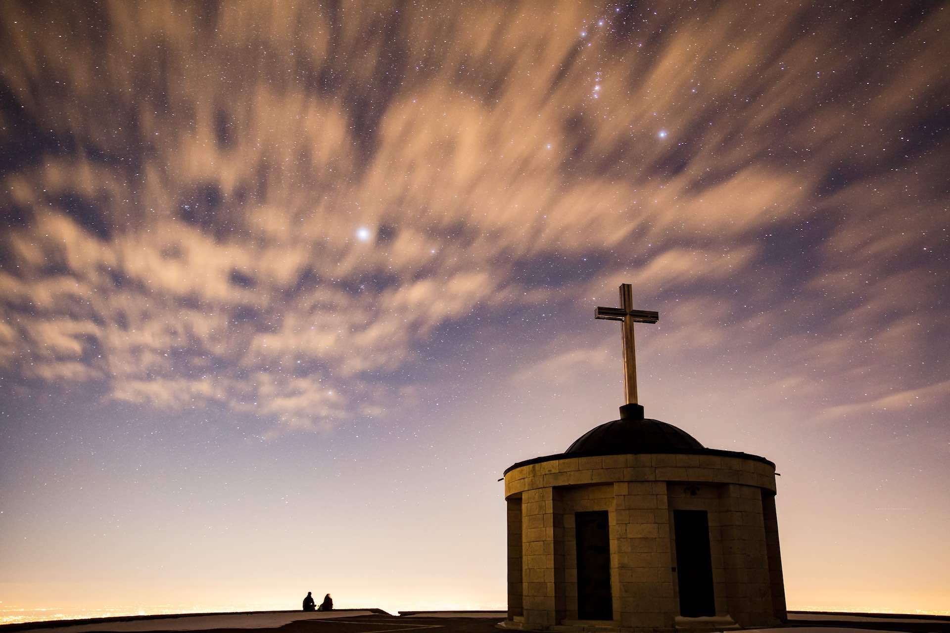 A chapel with crucifix silhouetted by a pink sky at dusk 