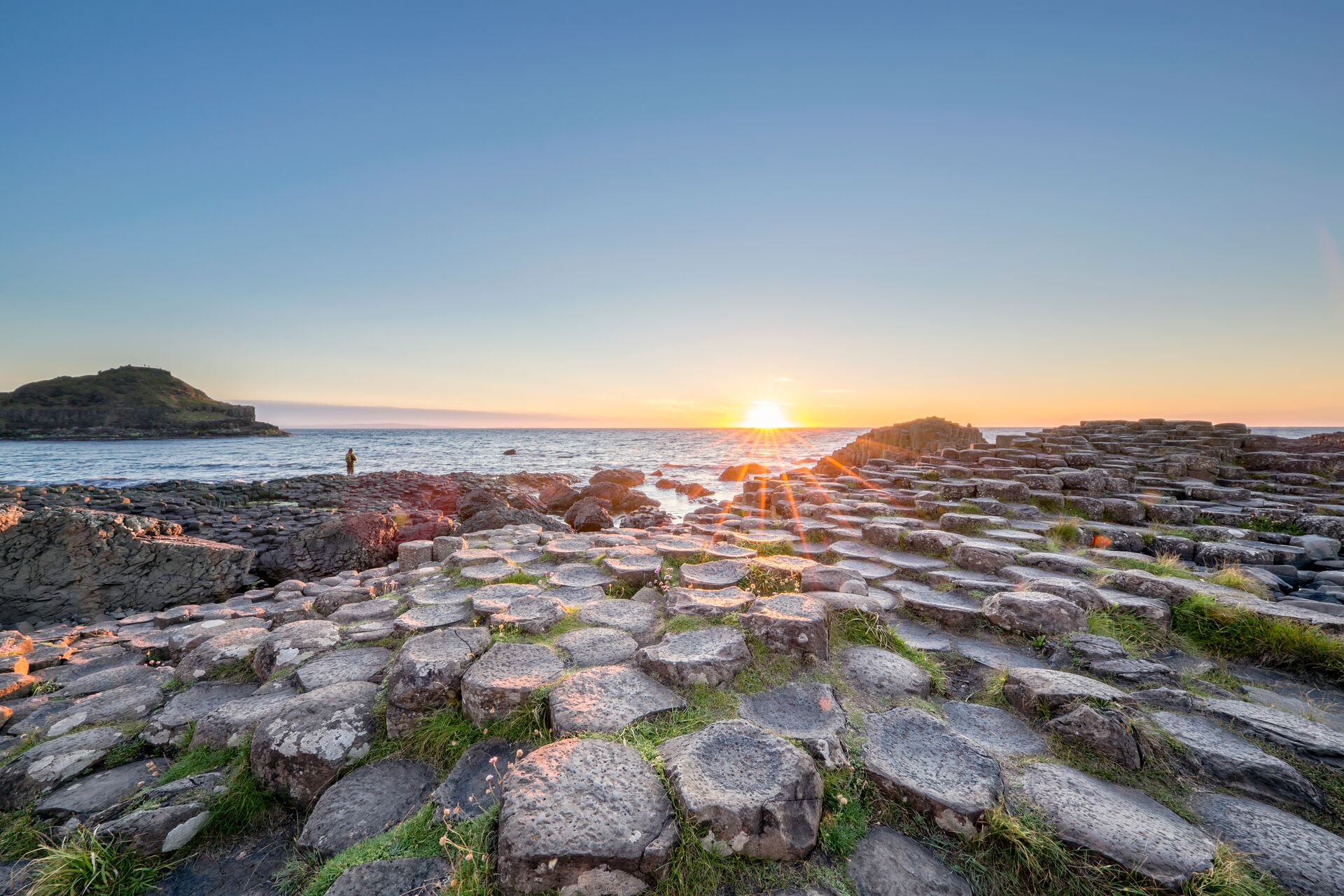 The hexagonal columns of the Giant’s Causeway are framed by a backdrop of se and the sun rising