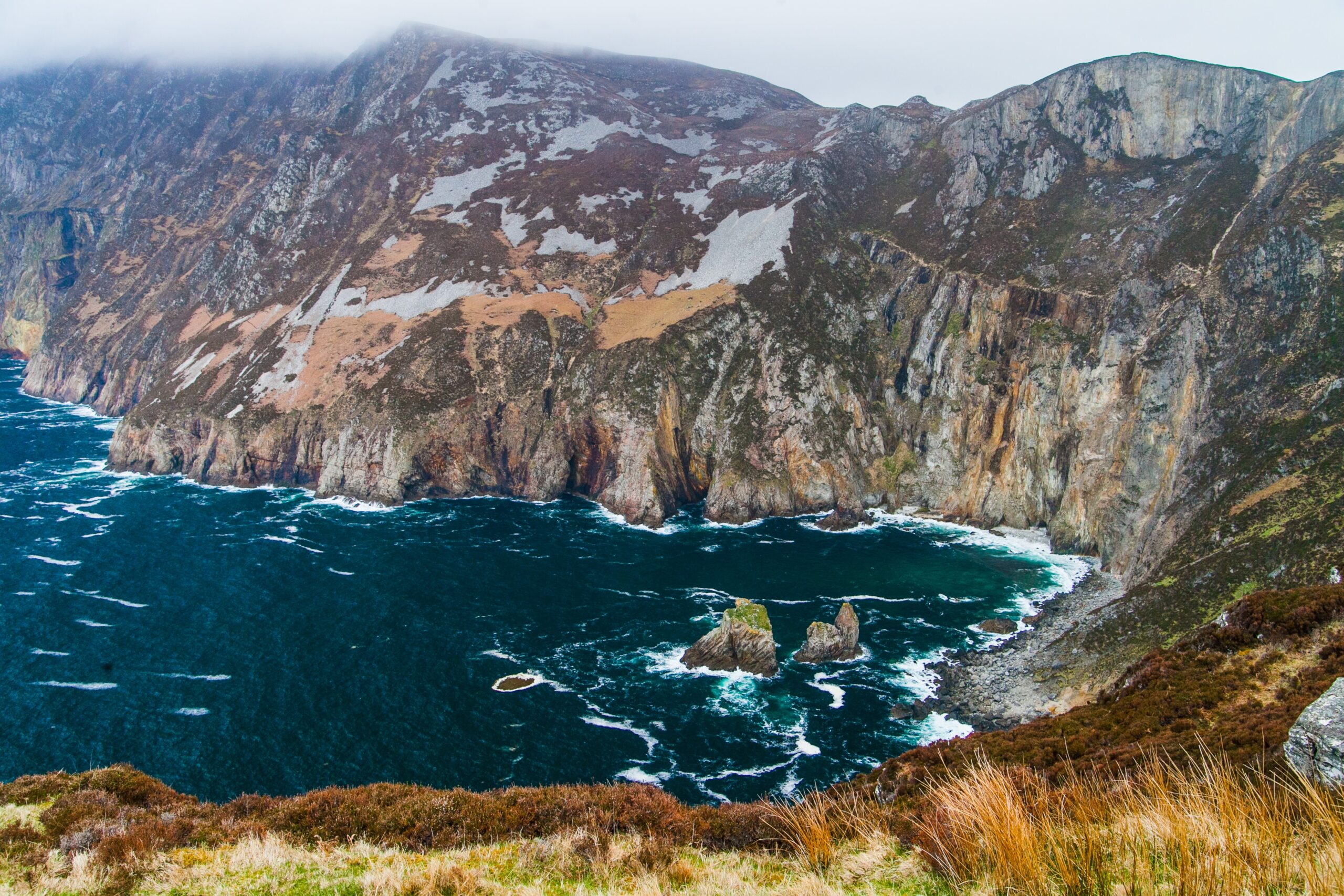 Grey craggy island cliffs drop into dark blue ocean waters